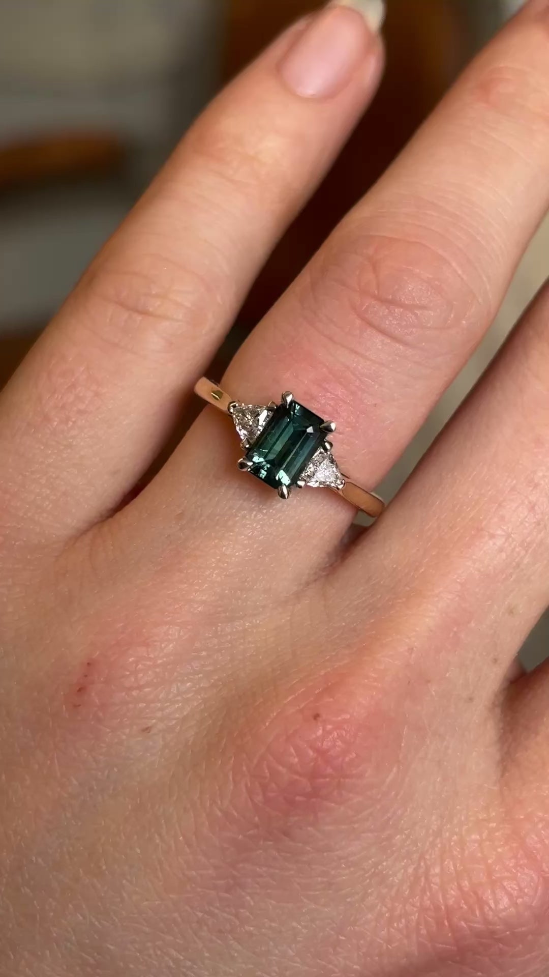 Green sapphire and diamond three-stone engagement ring on hand at a distance to show scale 