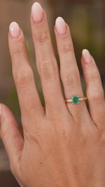  a video of a hand wearing a emerald engagement ring in yellow gold with diamond shoulders vintage in style. The hand slowly turns.