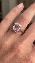 Antique-inspired sunset pink sapphire and diamond cluster engagement ring featuring an octagon-cut sunset pink sapphire surrounded by a halo of brilliant-cut diamonds, displayed on a hand.