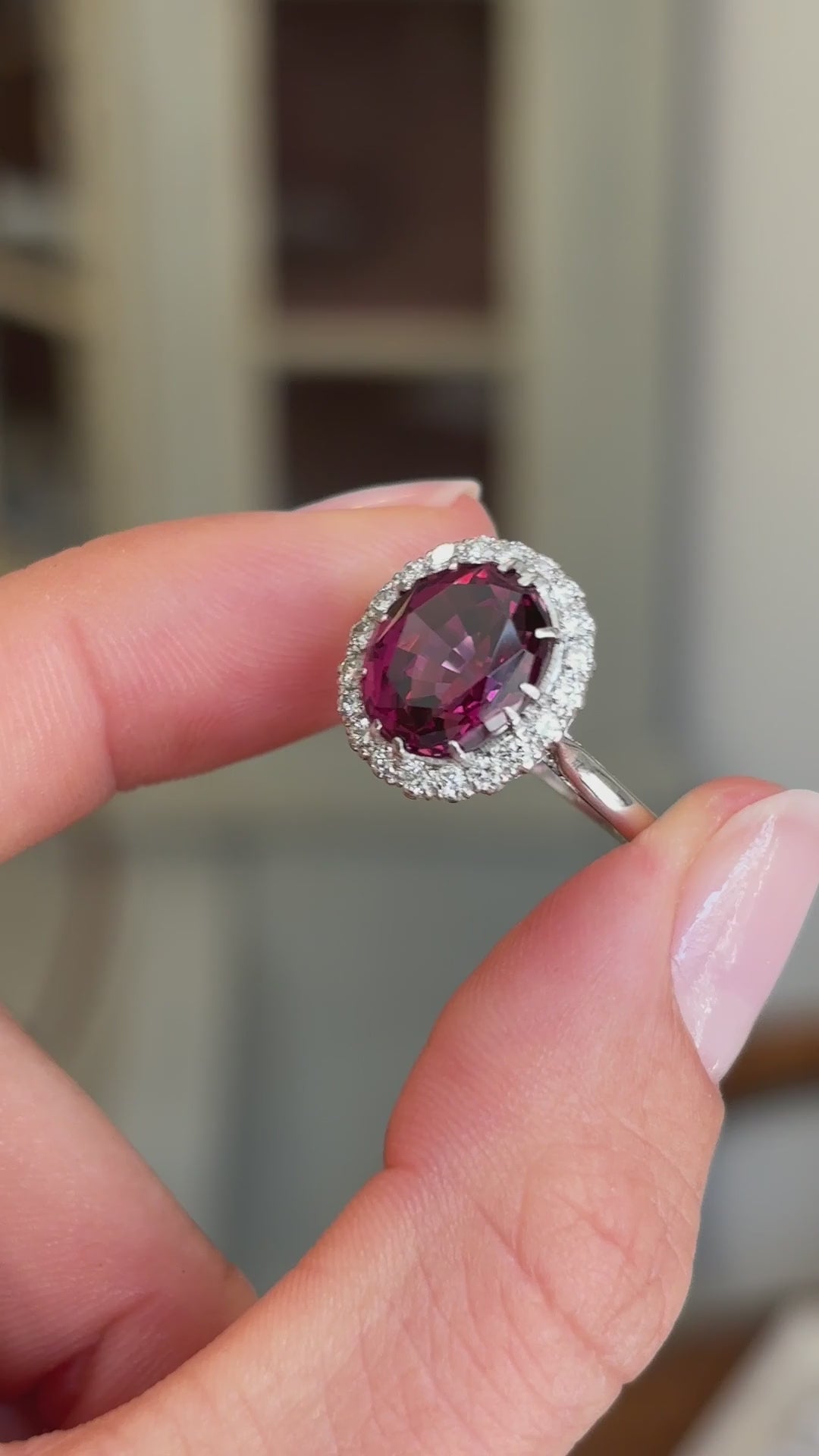 Vintage 1960s garnet and diamond cluster engagement ring featuring an oval garnet encircled by brilliant-cut diamonds, held by hand for detailed viewing.