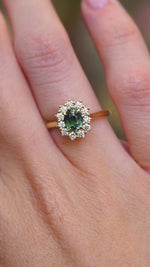 A video of an antique-inspired teal sapphire and diamond halo engagement ring in 14ct yellow gold worn on the hand.