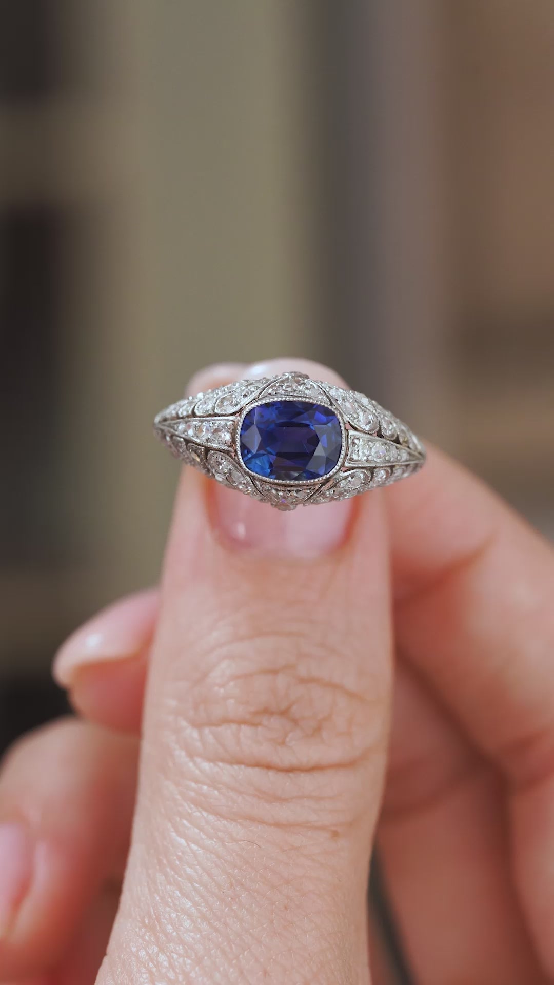 Video close-up of an antique sapphire ring balanced on a fingertip, revealing the dimensional diamond-set bombé construction.