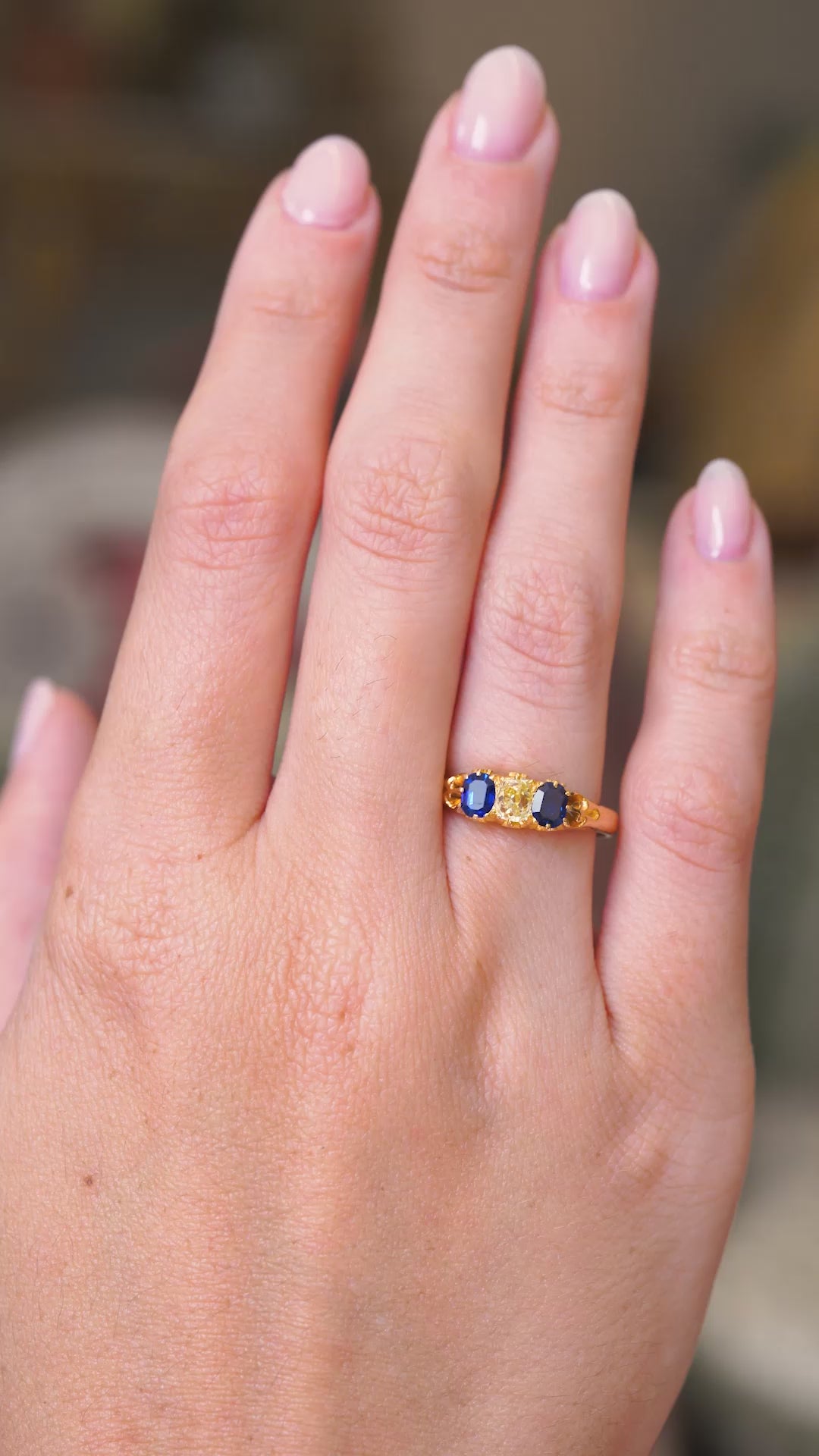 a video of an Antique, Victorian era dark blue sapphire and elongated cushion cut yellow diamond three-stone engagement ring in yellow gold worn on a hand whilst it slowly moves. 