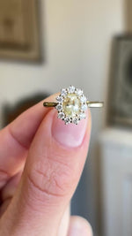 Antique-inspired yellow sapphire and diamond cluster engagement ring showcasing an oval yellow sapphire and diamond halo, held by hand to highlight the setting and profile.