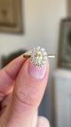 Antique-inspired yellow sapphire and diamond cluster engagement ring showcasing an oval yellow sapphire and diamond halo, held by hand to highlight the setting and profile.