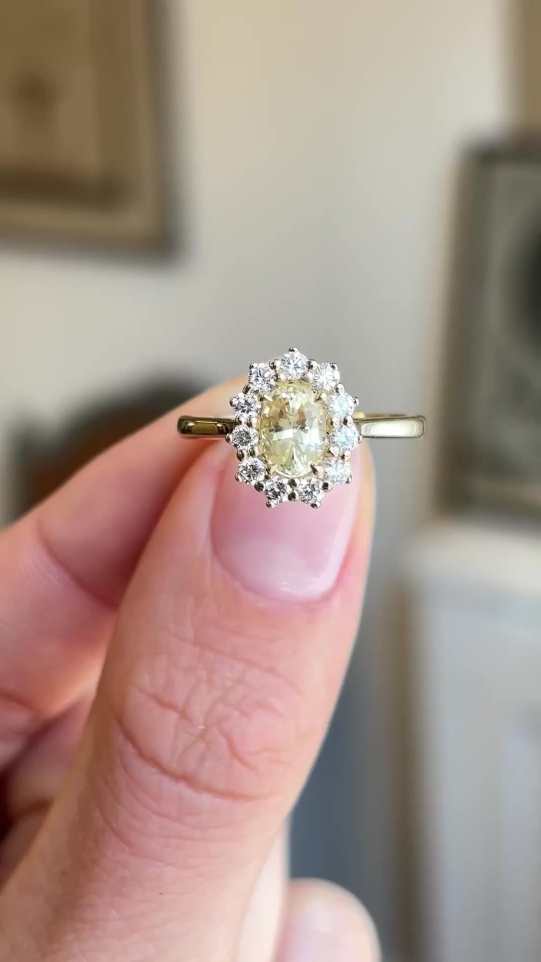 Antique-inspired yellow sapphire and diamond cluster engagement ring showcasing an oval yellow sapphire and diamond halo, held by hand to highlight the setting and profile.