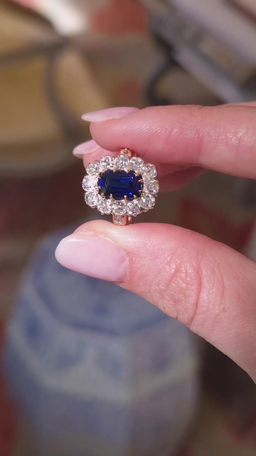Blue sapphire and diamond cluster ring held in between fingers and rotated to show different angles of the ring
