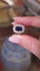 Blue sapphire and diamond cluster ring held in between fingers and rotated to show different angles of the ring