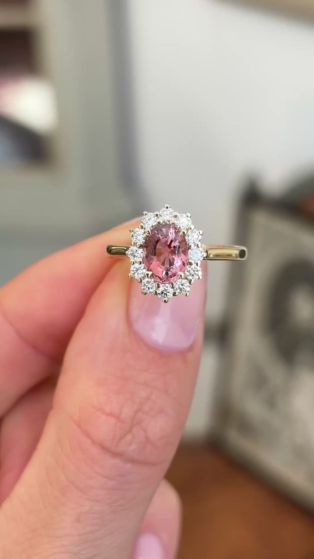 Antique-inspired rose-pink tourmaline and diamond cluster engagement ring featuring an oval rose-pink tourmaline and brilliant-cut diamond halo, held by hand to showcase the setting and craftsmanship.