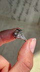 Antique Art Deco diamond cluster ring with a geometric diamond set cluster and intricate openwork detailing, held by hand and rotated to showcase the design.
