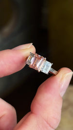 Lab-pink diamond and white diamond three-stone ring shown in natural light, revealing the sparkle and colour of the gemstones.