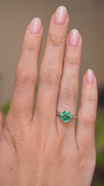 A video of a hand wearing a Vintage, 1990s emerald solitaire engagement ring on a wedding finger and rotated slowly to show the profile of the ring once worn on a finger. Against a softly blurred indoor setting. 