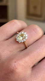 Antique-inspired yellow sapphire and diamond cluster engagement ring featuring an oval yellow sapphire surrounded by a halo of brilliant-cut diamonds, displayed on a hand.