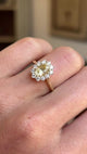 Antique-inspired yellow sapphire and diamond cluster engagement ring featuring an oval yellow sapphire surrounded by a halo of brilliant-cut diamonds, displayed on a hand.