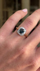 Antique Art Deco sapphire and diamond cluster engagement ring featuring a blue sapphire centre stone surrounded by a geometric diamond cluster, displayed on a hand.