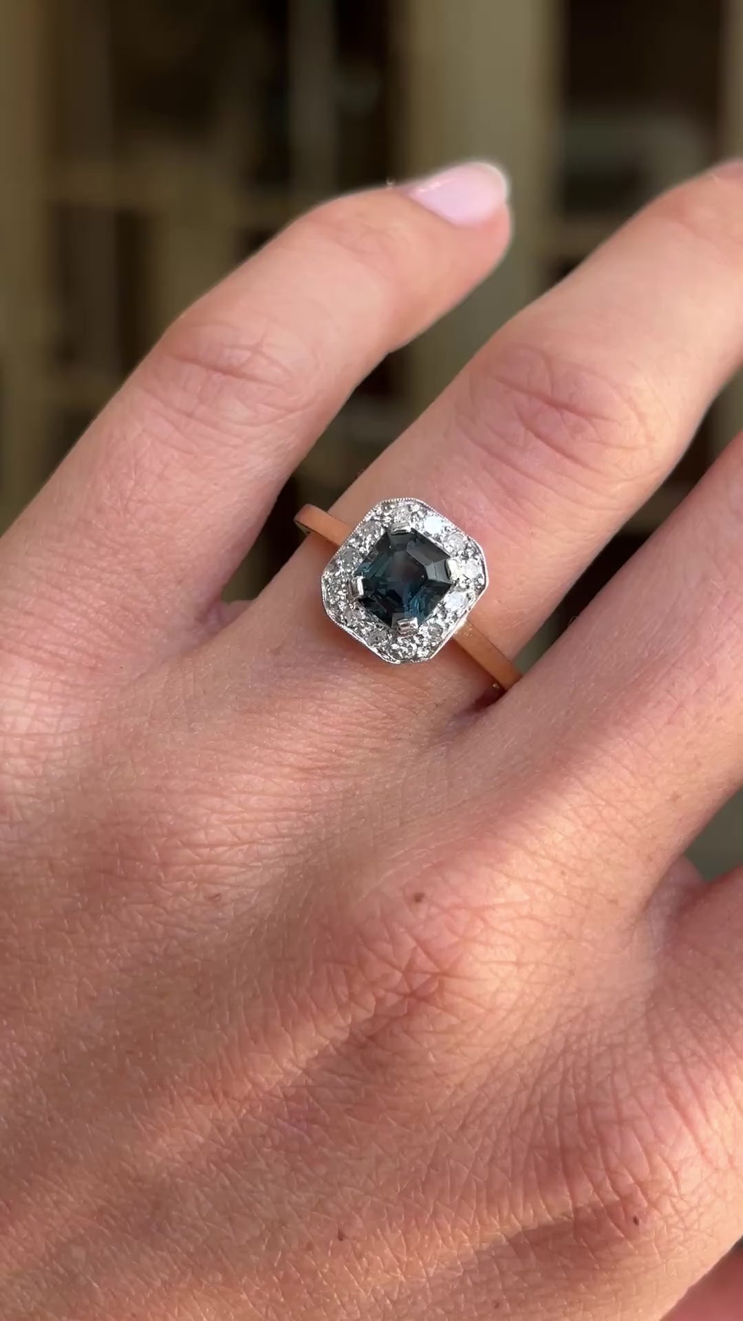 Antique Art Deco sapphire and diamond cluster engagement ring featuring a blue sapphire centre stone surrounded by a geometric diamond cluster, displayed on a hand.
