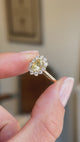 Antique-inspired yellow sapphire and diamond cluster engagement ring featuring an oval yellow sapphire encircled by brilliant-cut diamonds, held by hand for detailed viewing.