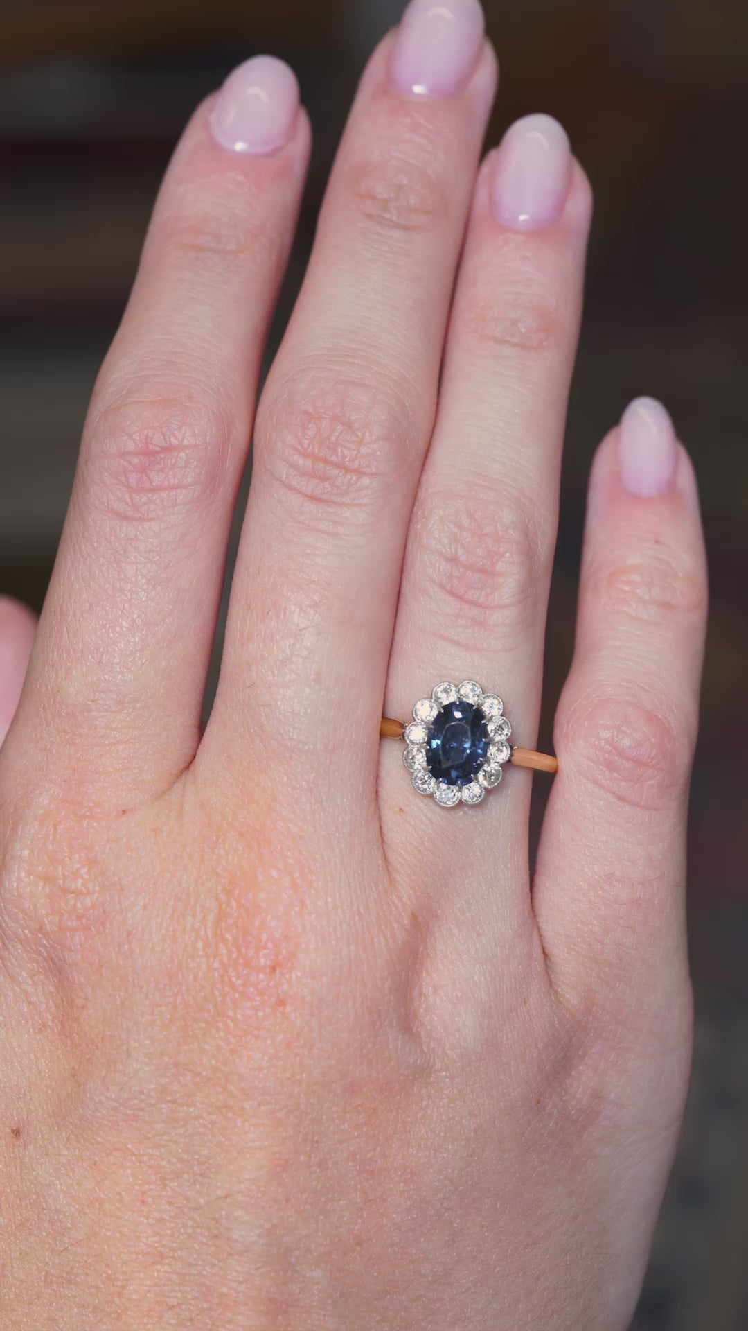 A video of an Antique, Edwardian blue spinel and diamond cluster engagement ring in yellow gold being worn on an outstretched hand as it gently moves. 