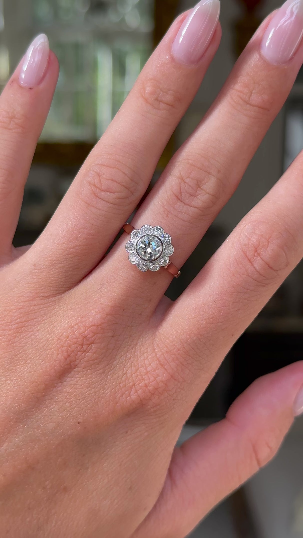 antique diamond cluster engagement ring, worn on hand and moved away from lens to give perspective, front view.