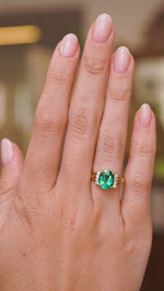 A video of a Vintage, 1970s emerald and diamond engagement ring worn on a wedding finger and rotated slowly to show how the profile of the ring looks on a hand and showcasing the yellow gold band. 