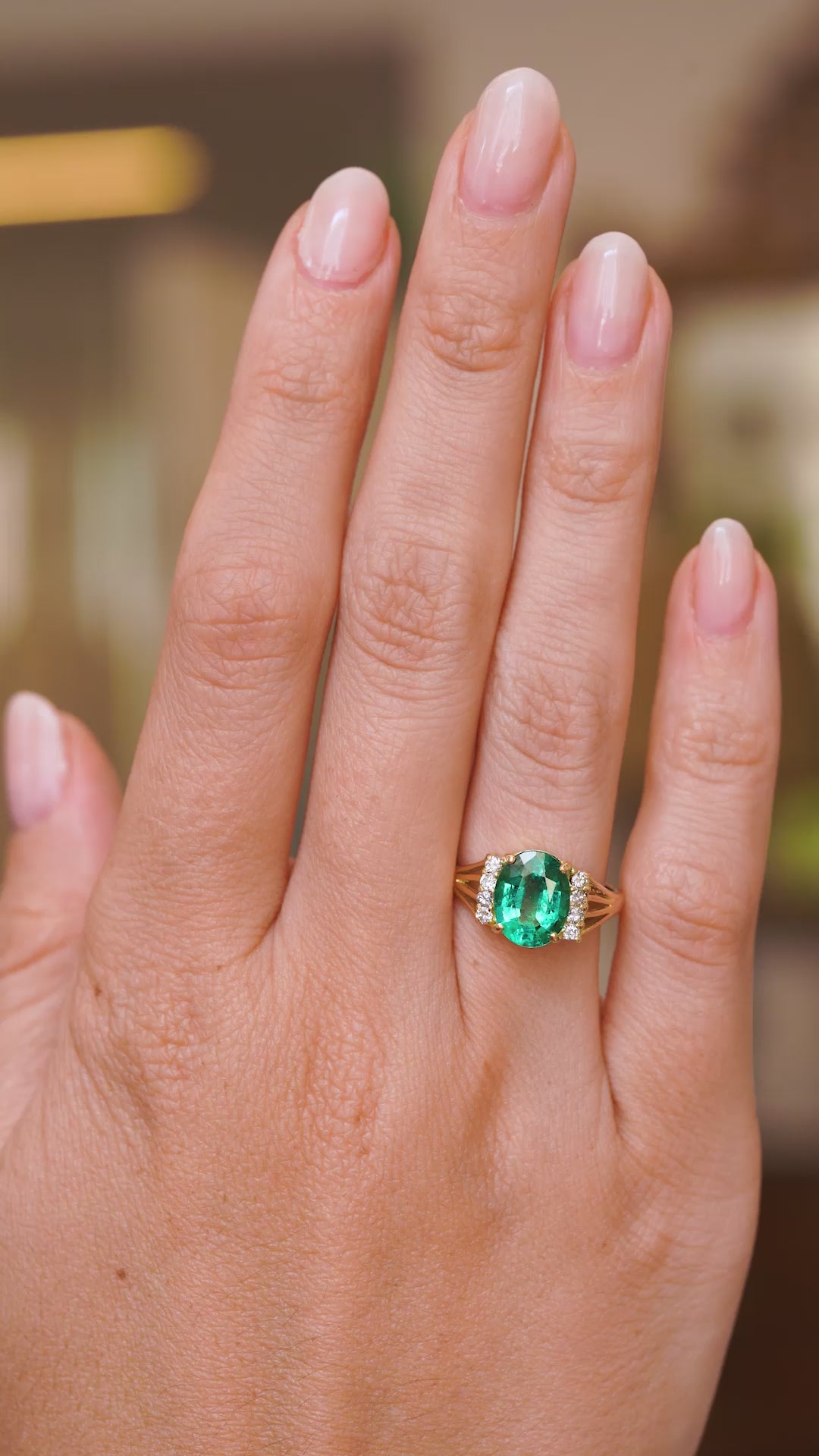 A video of a Vintage, 1970s emerald and diamond engagement ring worn on a wedding finger and rotated slowly to show how the profile of the ring looks on a hand and showcasing the yellow gold band. 