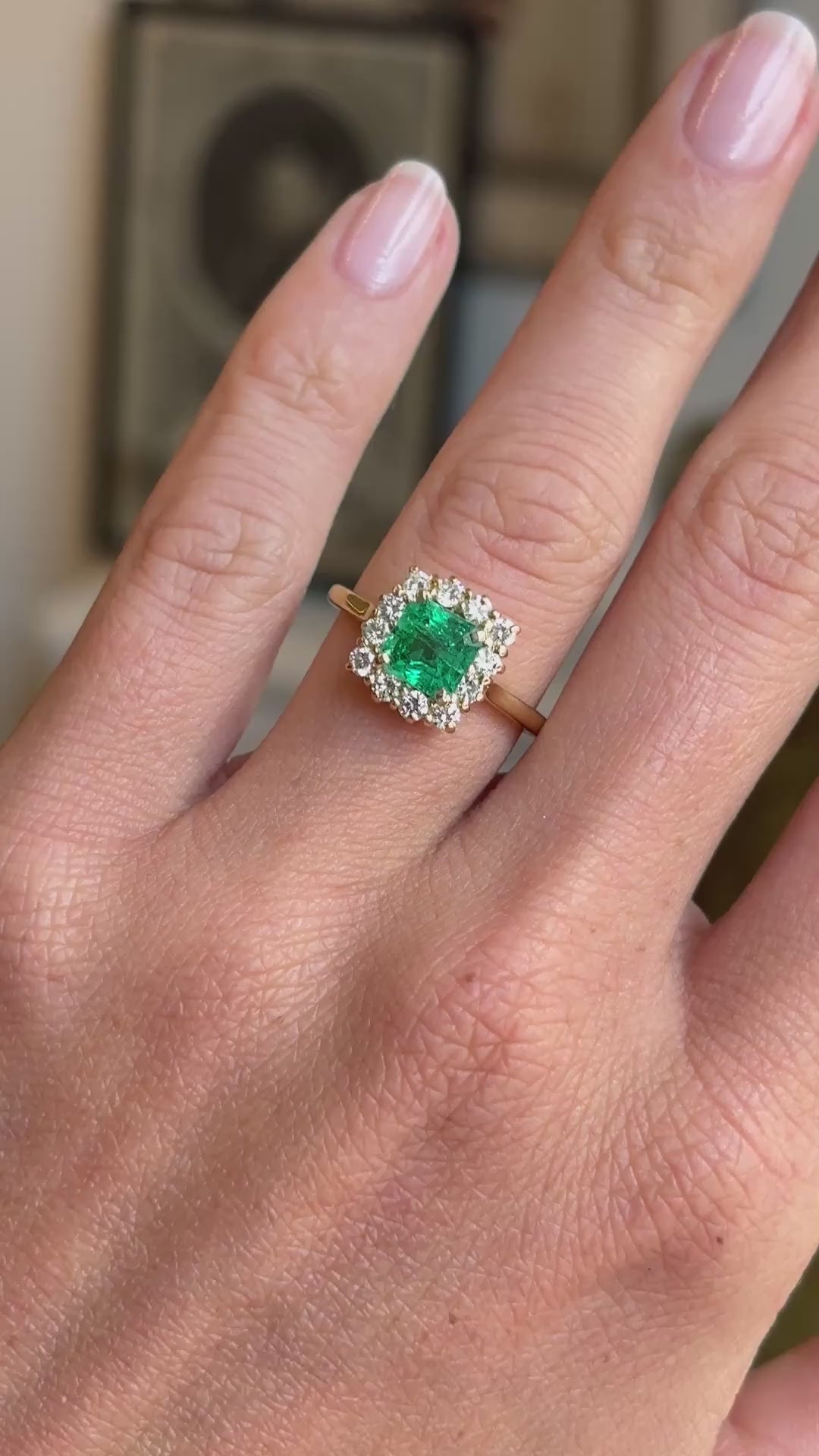 Vintage 1980s Colombian emerald and diamond cluster engagement ring featuring an emerald-cut Colombian emerald encircled by brilliant-cut diamonds, held by hand for detailed viewing.