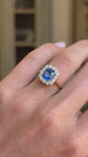 Video of an antique-inspired violet-blue cushion cut Sri Lankan sapphire and diamond cluster engagement ring in yellow gold worn on hand, showcasing the richly coloured sapphire, sparkling diamond halo and elegant antique-inspired design against a warm vintage interior backdrop.
