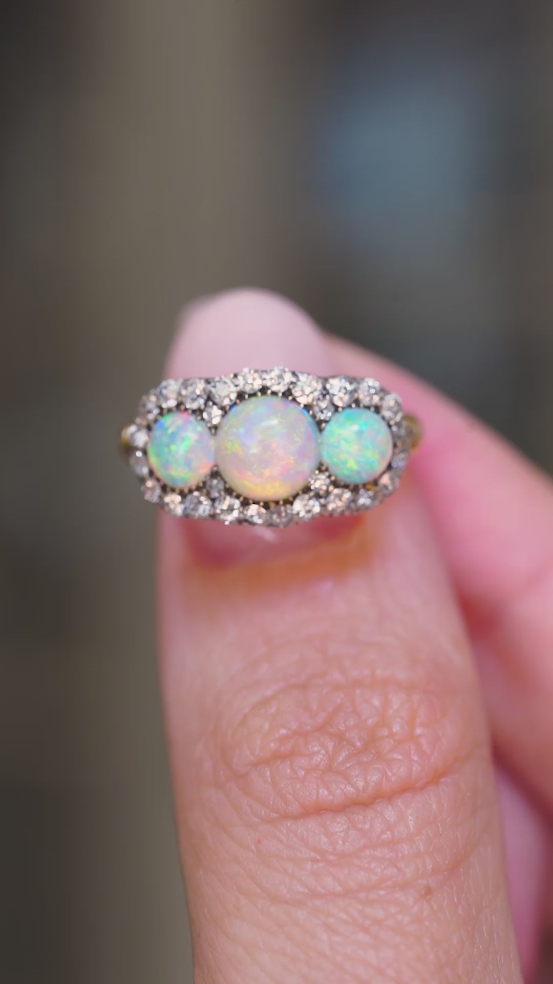 A close-up  video of an antique three-stone round opal & diamond cluster ring shown between fingers.