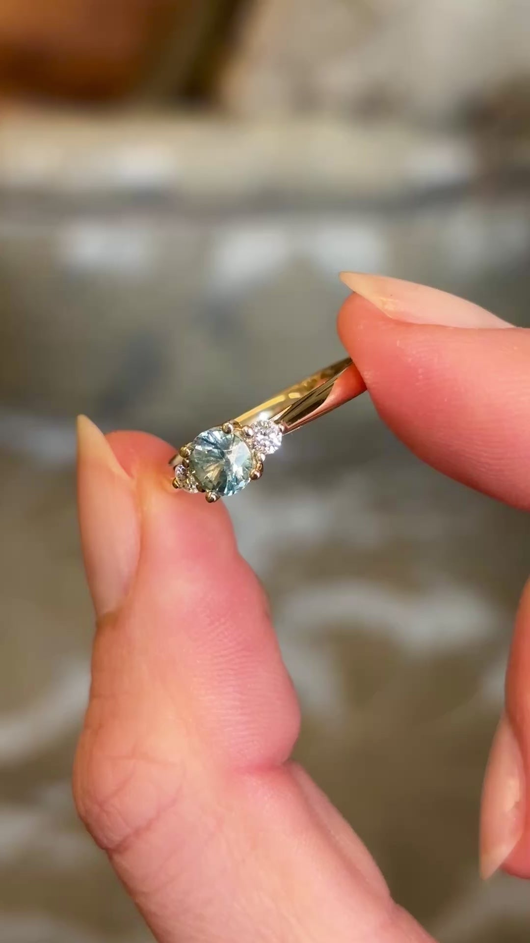 Round-cut teal sapphire and diamond three-stone engagement ring captured in natural light, highlighting the sparkle and colour of the gemstones.