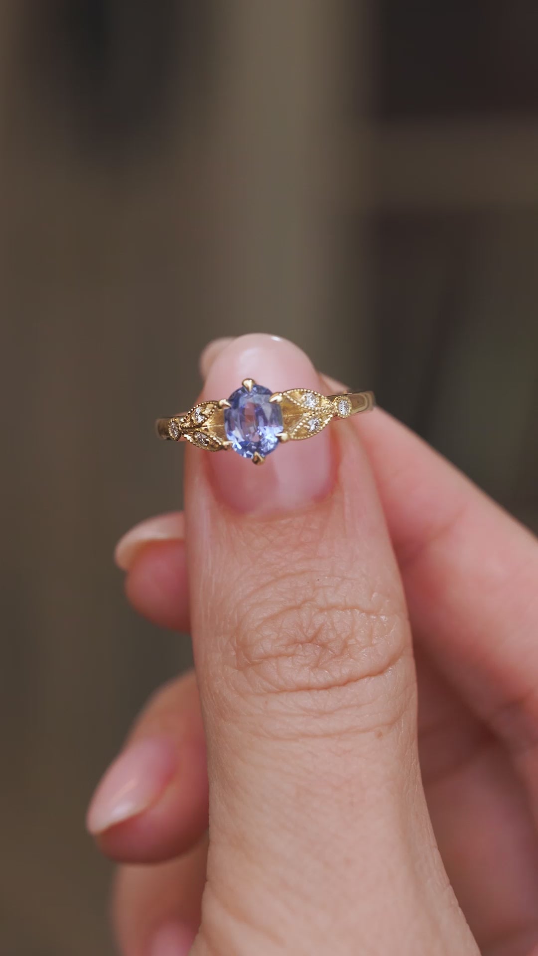 Video presenting the vintage-inspired sapphire engagement ring balanced on a fingertip for a clear view of its ornate shoulders.