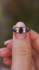 A close up video of an Antique, Edwardian blue sapphire and diamond five-stone engagement ring held between two fingers and rotated slowly to show the detailed gold work of the setting and the profile of the yellow gold band. 