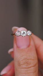 A video of an Antique, Edwardian diamond three-stone engagement ring in yellow gold held between fingers against a blurred background