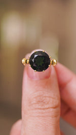 A close up video of a Vintage, 1980's green tourmaline cocktail ring, showcasing the central stone and yellow gold setting and band.  Held between two fingers and rotated slowly to show the side profile. 