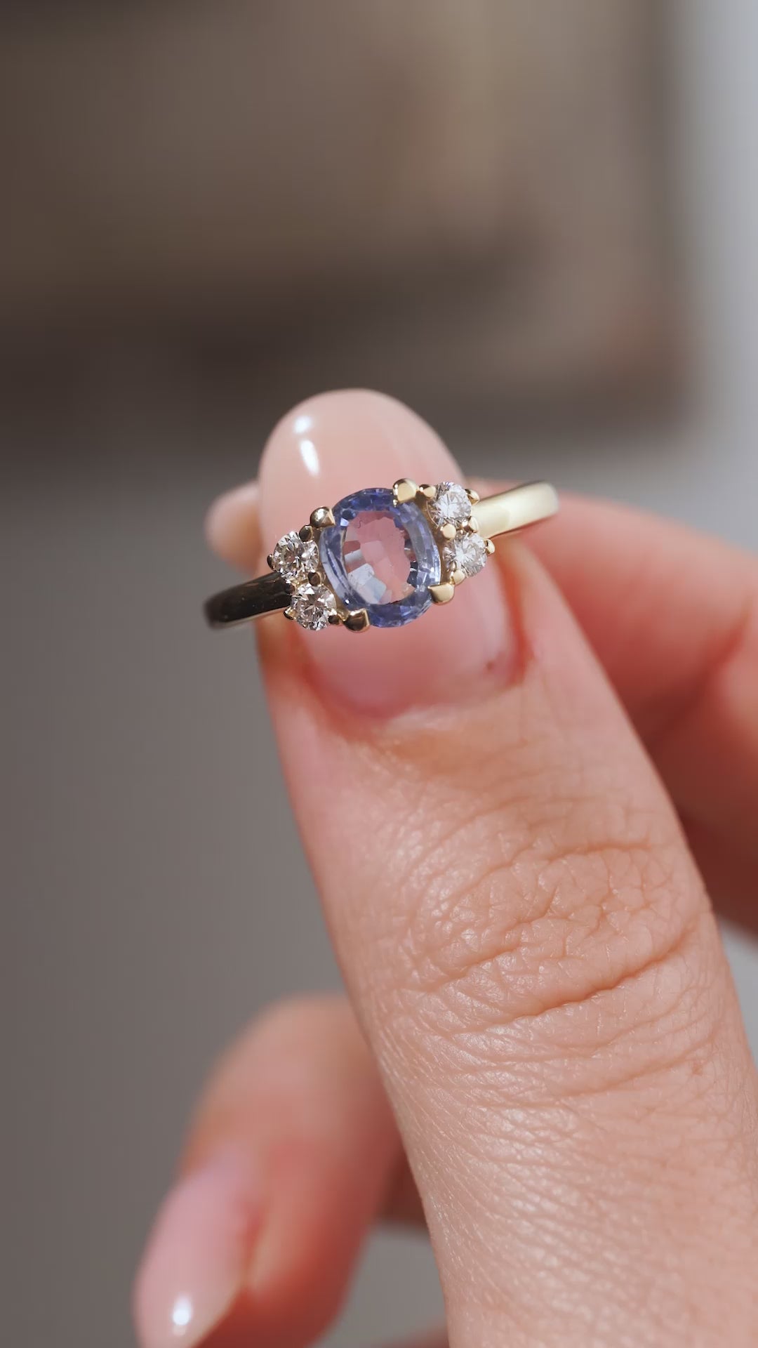 A close-up video of the vintage-inspired blue sapphire and diamond ring held between fingers, capturing the gemstone's soft blue facets and sparkling diamond accents.
