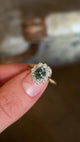 Green sapphire and diamond cluster engagement ring held in fingers and rotated to show details. 