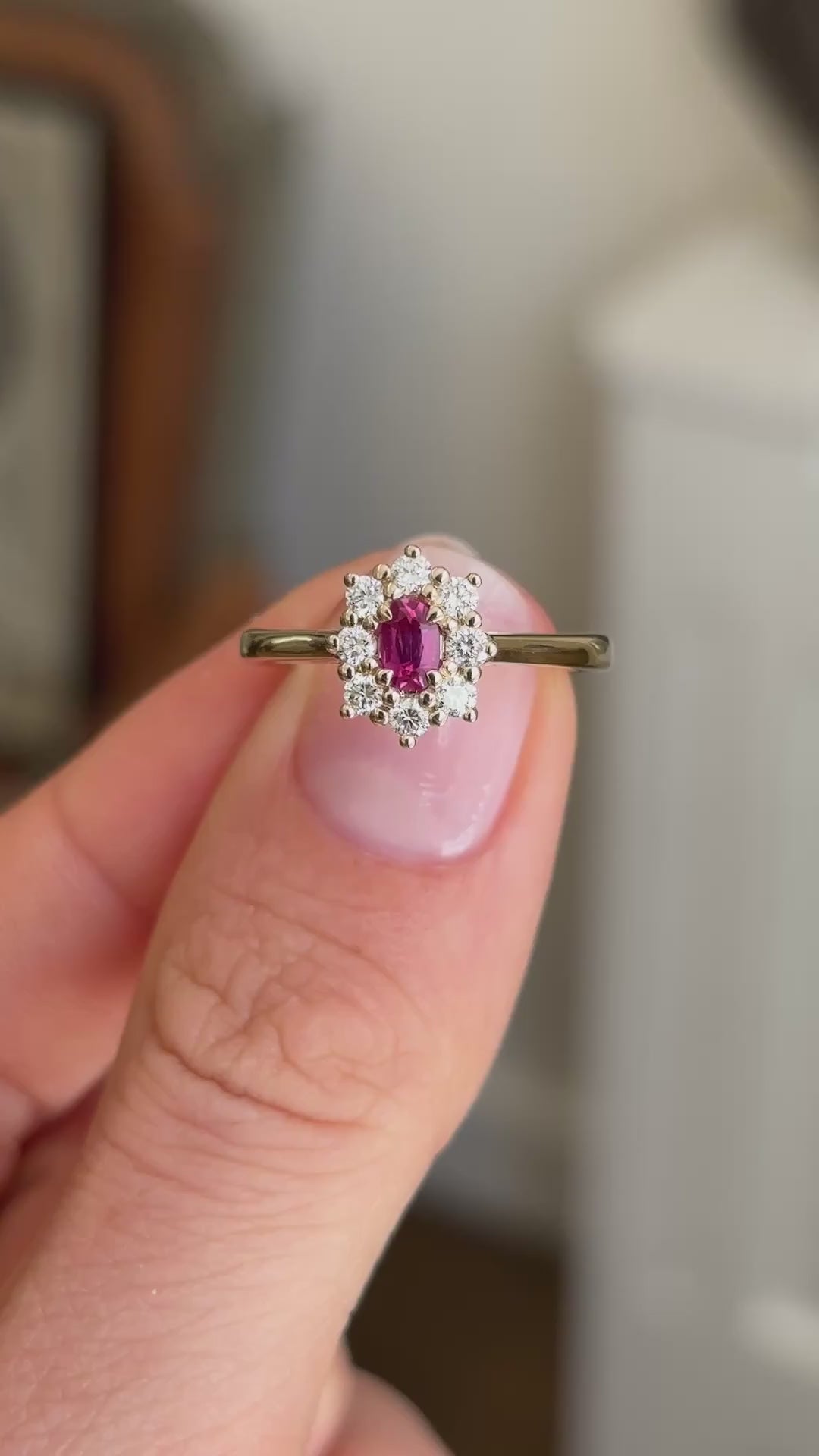 Antique-inspired yellow gold ruby and diamond cluster ring worn on hand, featuring an oval-cut ruby surrounded by brilliant diamonds, filmed against a softly lit vintage interior backdrop.