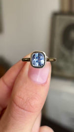 Close up video of an Antique-inspired, light purple coloured cushion-cut sapphire solitaire engagement ring in yellow gold, held between two fingers and rotated slowly to display all the profiles of the ring. 