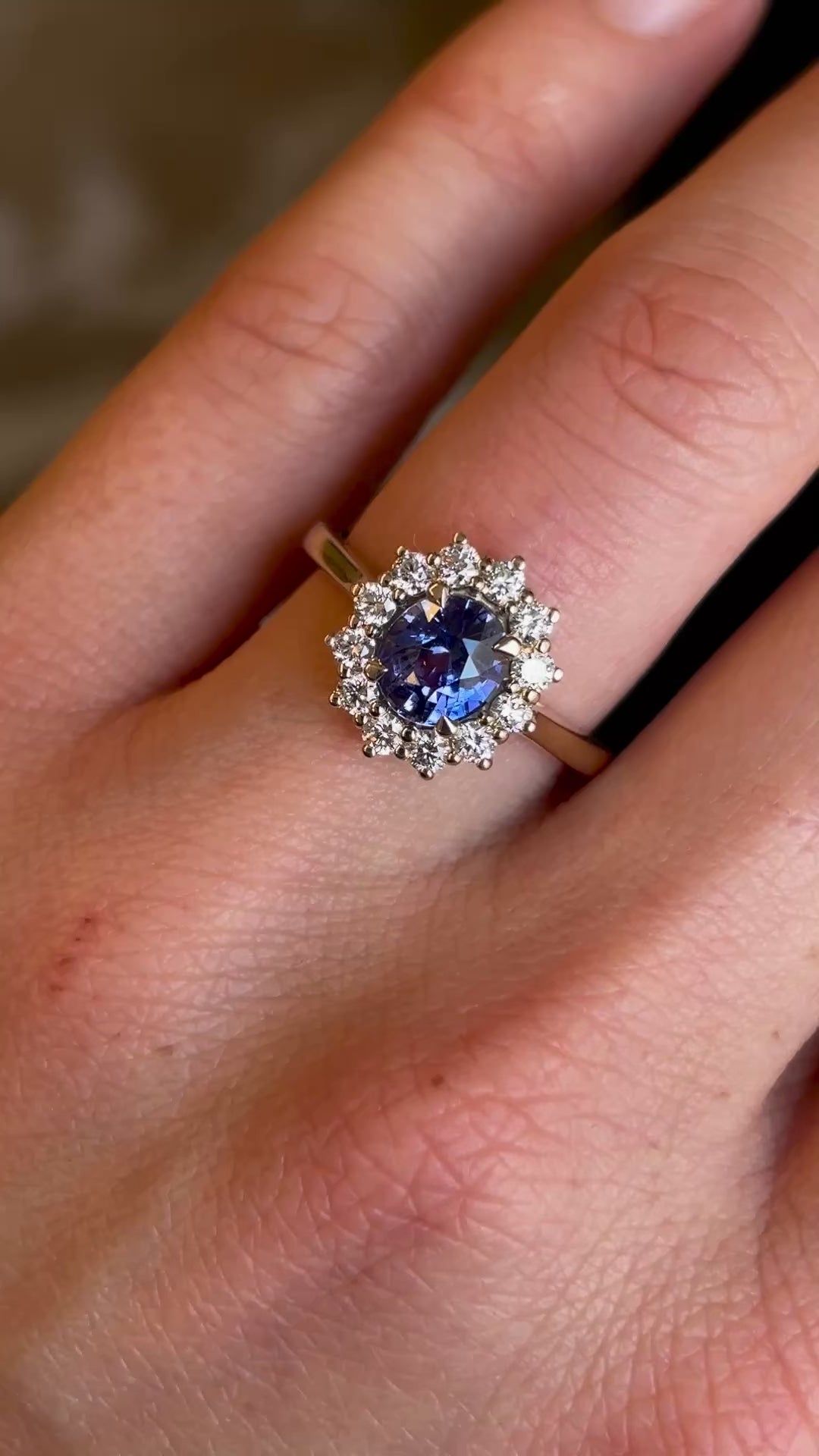 Blue sapphire and diamond cluster engagement ring worn on hand in video to show sale and proportion. 