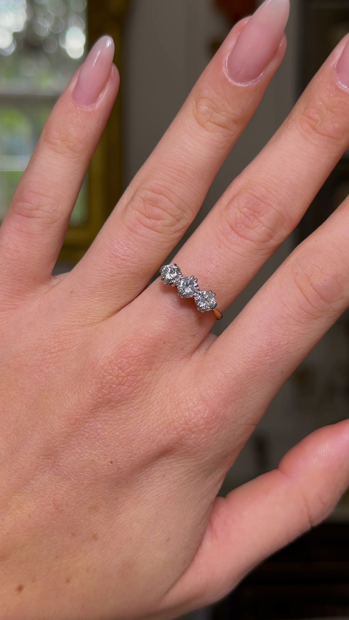 three stone diamond engagement ring, worn on hand and moved away from lens to give perspective, front view.