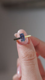 A close-up video of the antique-inspired sapphire solitaire held between fingers, displaying its rectangular step-cut facets and delicate gold claws.