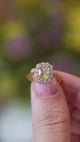 Pale yellow sapphire and diamond cluster engagement ring held between fingers showing a subtle sparkle.