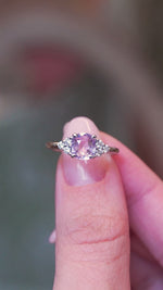 Pink sapphire and diamond cluster tre-foil engagement ring with diamond side clusters held between fingers showing ring details.