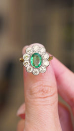 A vintage 1950s yellow and white gold ring with a green emerald gemstone and diamond cluster ring being shown in video between fingers. 