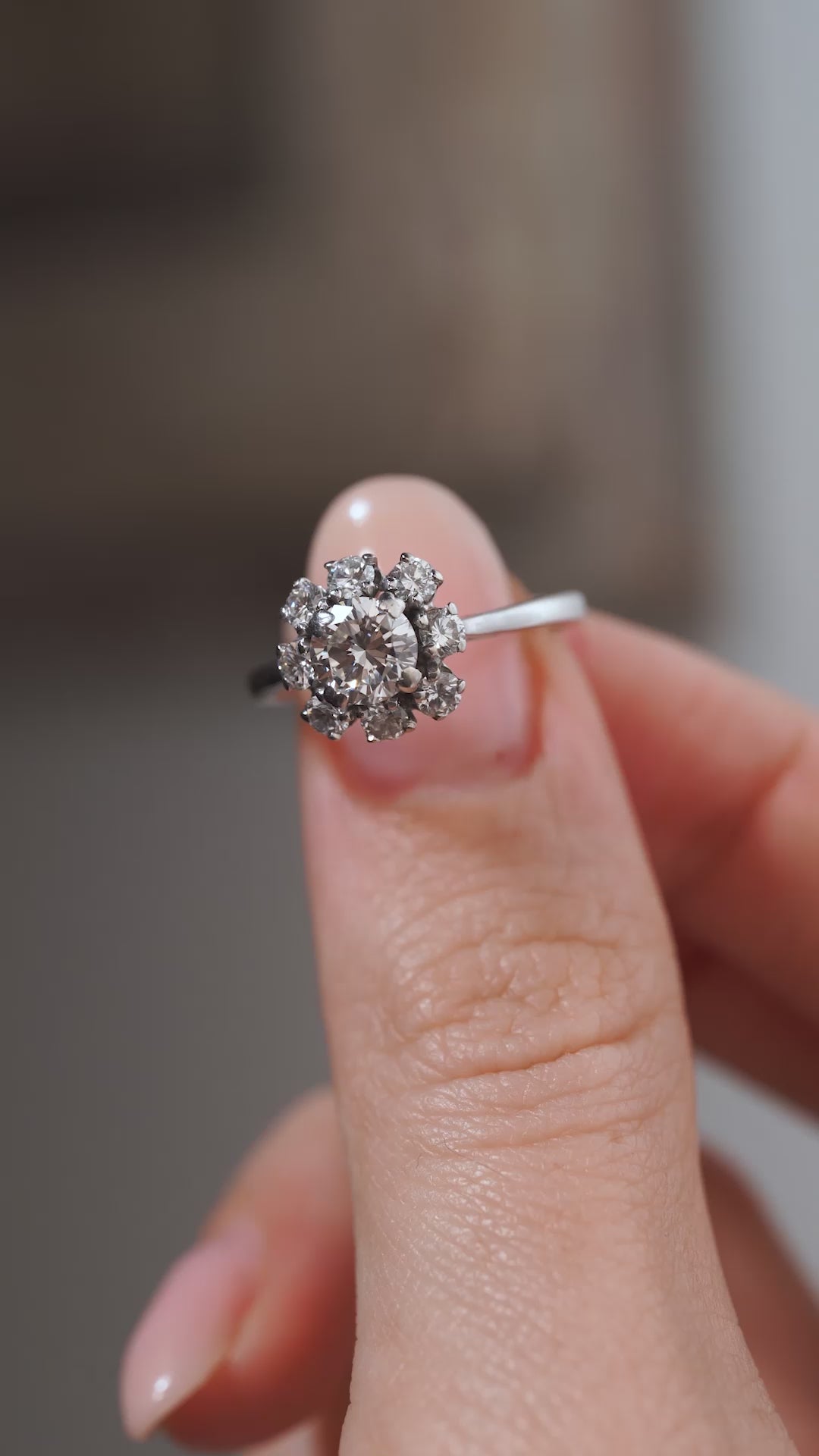 A close-up video of a vintage 1950s diamond cluster engagement ring held between fingers, displaying its sparkling diamond flower cluster and slim polished white gold band.