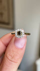 Video of a ring held between two fingers and rotated slowly to showcase the central square cut brown green diamond and halo of diamonds surrounding it.  Set in a yellow gold band and inspired by Antique designs.