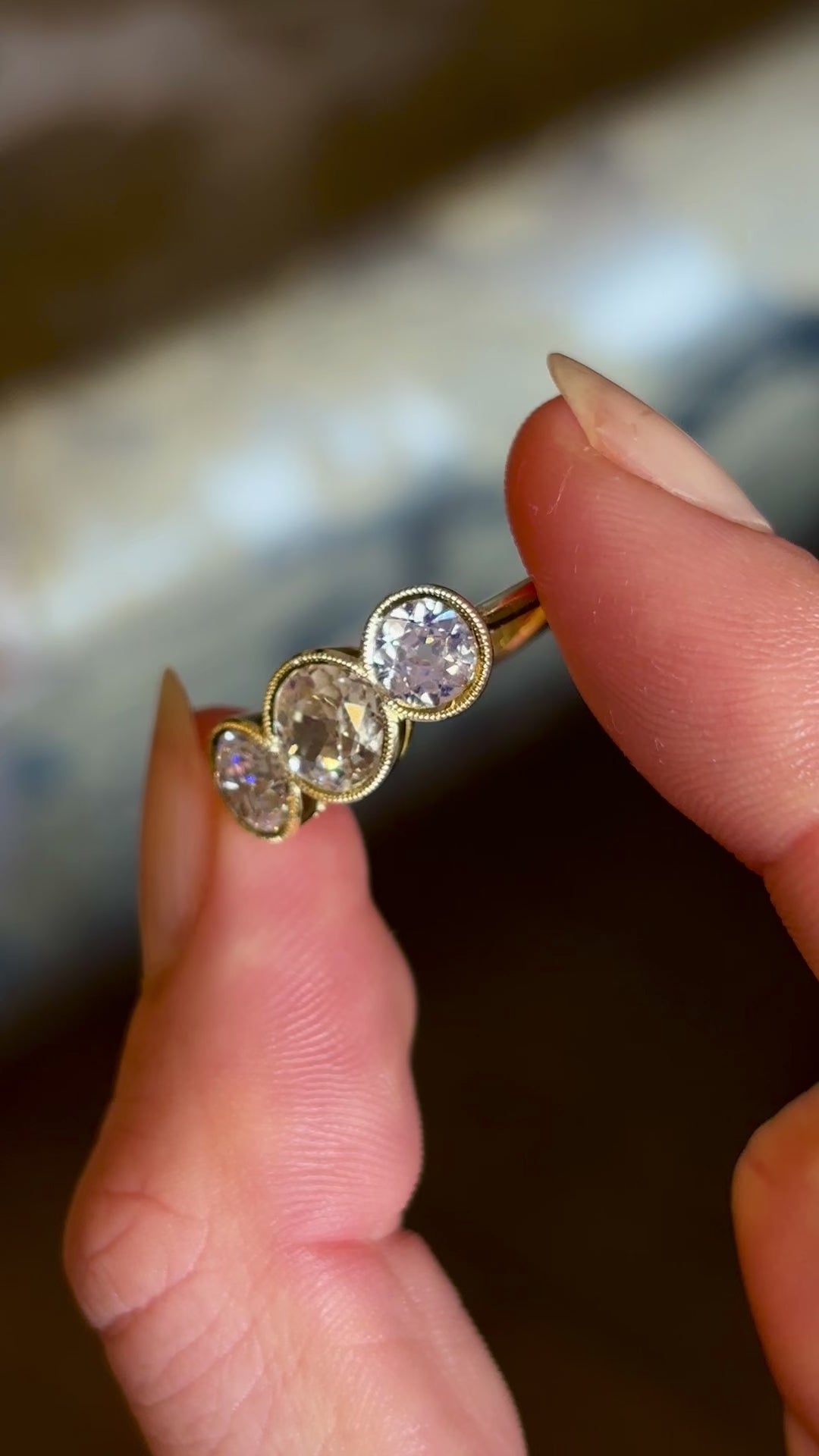 Antique, Victorian three-stone diamond ring held in fingers and slowly turned to show fine details. 