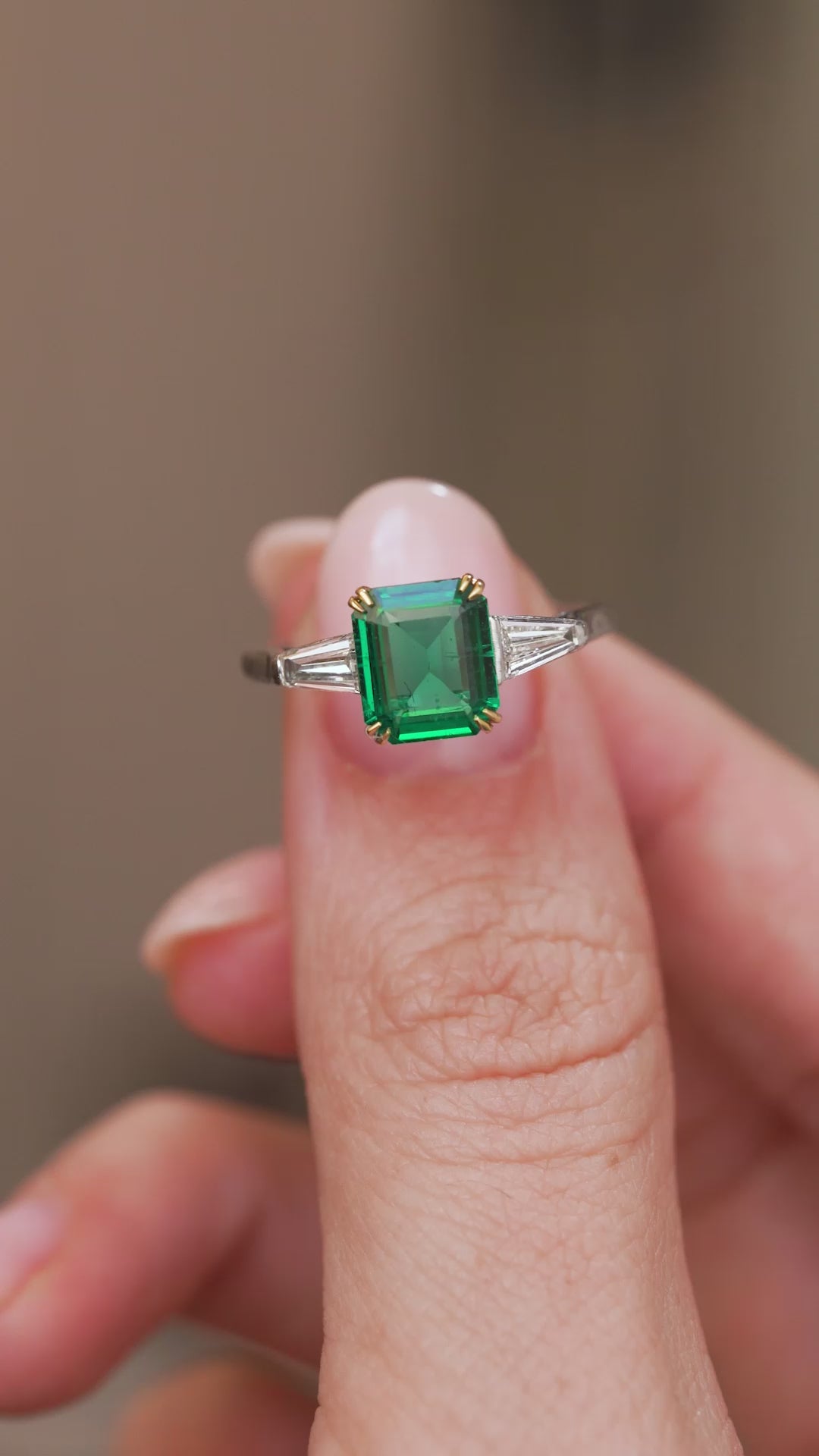 Video presenting the emerald three-stone ring balanced on a fingertip for a clear face-on look at its Art Deco-inspired geometry.