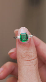 Video presenting the emerald three-stone ring balanced on a fingertip for a clear face-on look at its Art Deco-inspired geometry.