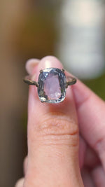 A video of a sapphire solitaire ring held in between fingers and turned to show various angles of the ring against a blurry background.