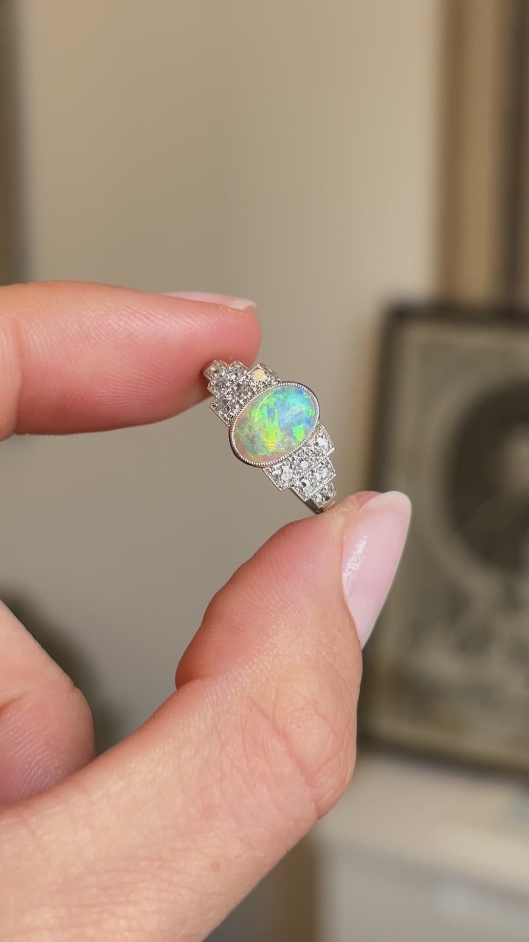 Detailed video of an antique Art Deco opal and diamond cluster ring held between fingers, displaying the opal's vibrant flashes of colour and elegant cluster design.